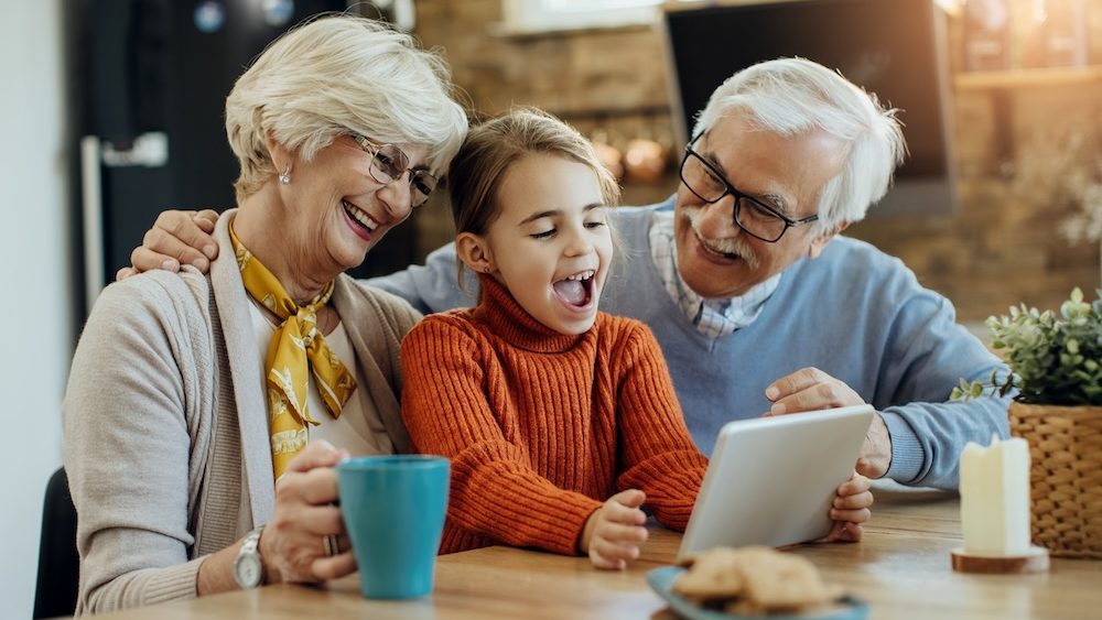 Happy little girl having fun while using digital tablet with her grandparents at home.