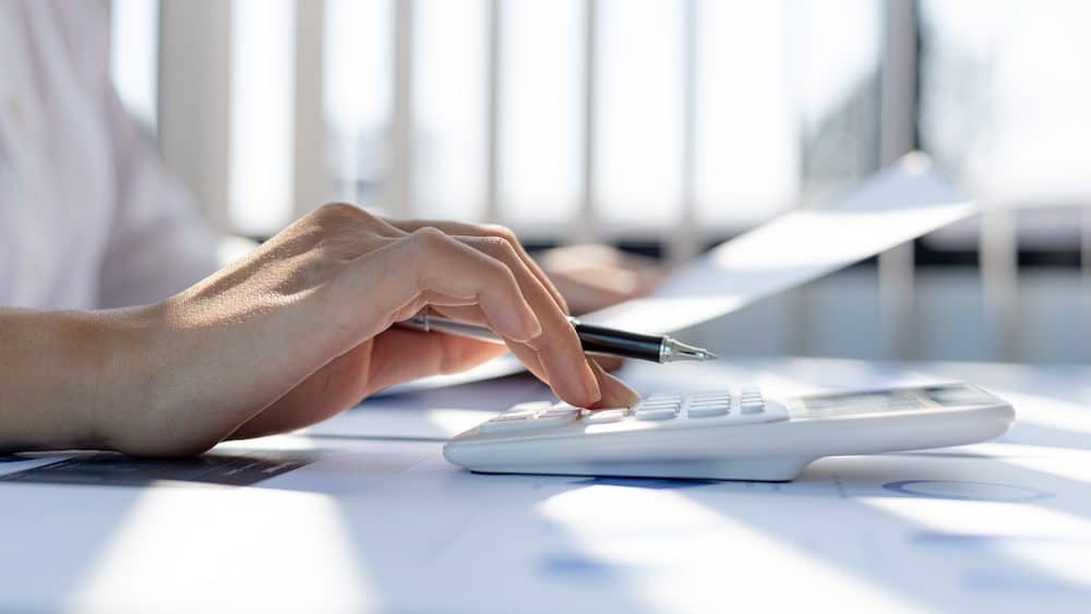 A business woman using a calculator to calculate numbers on a company's financial documents, she is analyzing historical financial data to plan how to grow the company. Financial concept.